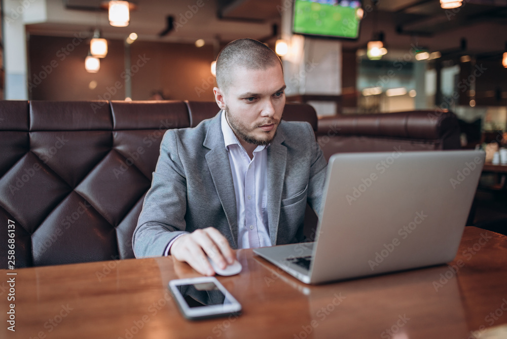 Handsome young businessman in jacket with a beard is sitting in cafe with laptop. Buisness process Handsome young businessman in jacket with a beard is sitting in cafe with laptop. Buisness process