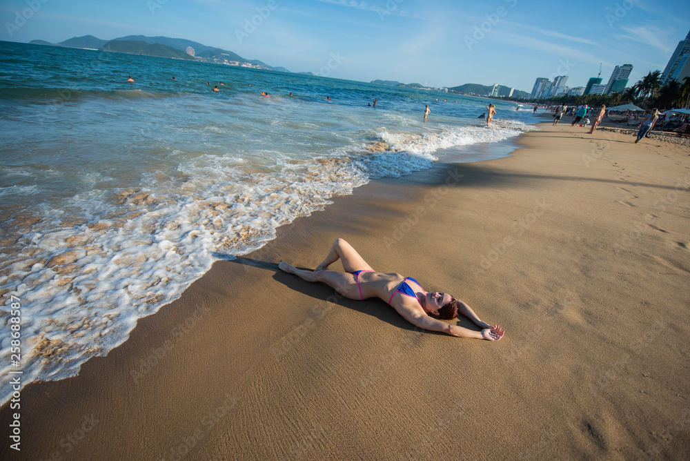 A young woman in a seductive bikini lying on the beach. Girl lying on the sand by the ocean A young woman in a seductive bikini lying on the beach. Girl lying on the sand by the ocean