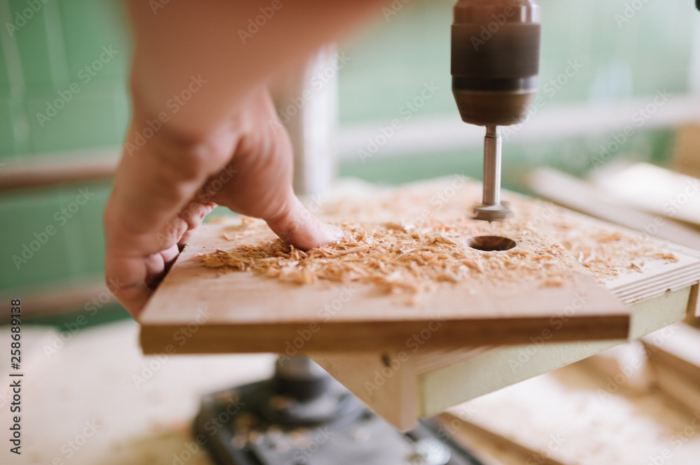 The master works on the machine for drilling in the carpentry workshop