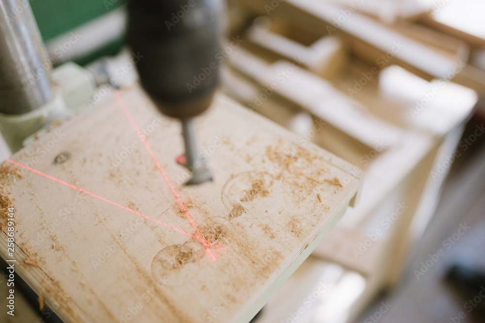 The master works on the machine for drilling in the carpentry workshop