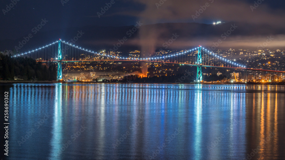 Fototapeta premium Vancouver, British Columbia. Canada Long exposure from below of the Lions Gate Bridge with lights trail, glitters and clouds.
