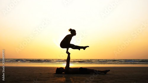 Silhouette of fit sporty couple practicing acrobatic yoga with partner together on the beach.