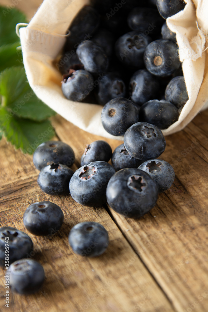 Blueberries spilling out of a brown textile, eco bag over rustic wood table. Zero waist concept, no plastic. Eco friendly berries, fruits. Bio berry. Blueberries spilling out of a brown textile, eco bag over rustic wood table. Zero waist concept, no plastic. Eco friendly berries, fruits. Bio berry.
