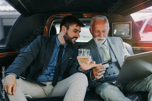 Senior businessman and his assistant sitting in limousine and celebrating their job success.