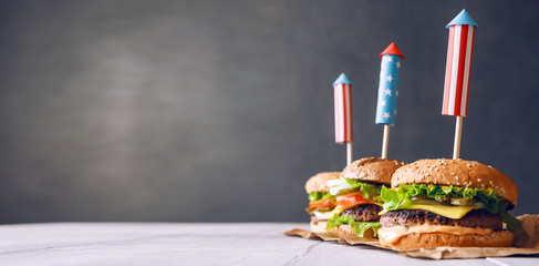 three fresh and juicy burgers with American flag-style fireworks inserted into them. bbq concept picnic to celebrate independence day