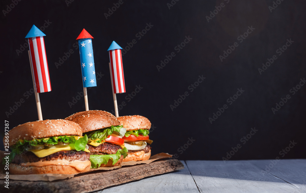 three fresh and juicy burgers with American flag-style fireworks inserted into them. bbq concept picnic to celebrate independence day
