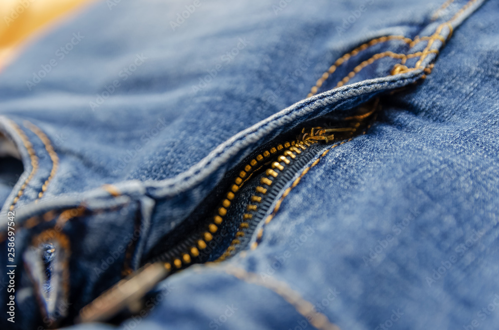 Close up image of a blue denim jeans with its metal zipper or fly open and  zipper tape metallic puller, bridge, slider body and chain visible along  with brown stitching Stock Photo