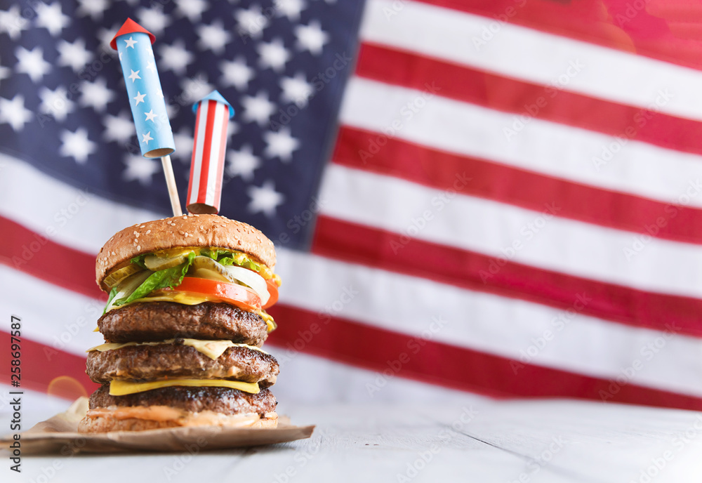 a big burger with three juicy beef patties bonded with American flag firework skewers. burgar concept for the day of independence day celebration of fourth of july - obrazy, fototapety, plakaty 