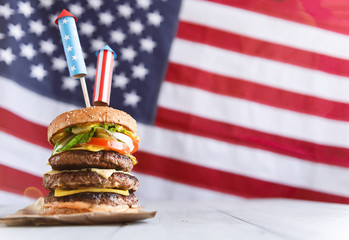 a big burger with three juicy beef patties bonded with American flag firework skewers. burgar concept for the day of independence day celebration of fourth of july