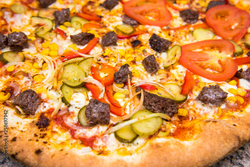 Fresh pizza on thin dough with tomatoes, beef, pickled cucumber, corn and red pepper