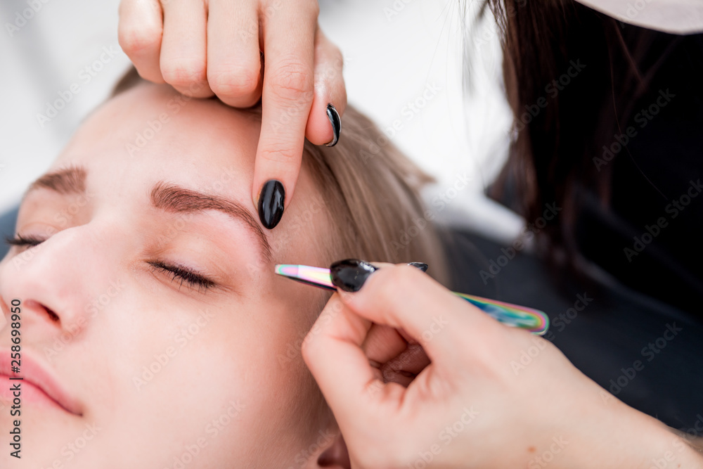Plucking eyebrows with tweezer by beautician at beauty salon Plucking eyebrows with tweezer by beautician at beauty salon
