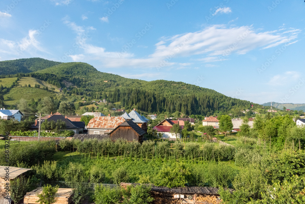 Beautiful countryside in romana, farms and old wooden houses with gardens. Cabins and barns at the foot of the mountains. Cloudy blue sky. Lawns and forests