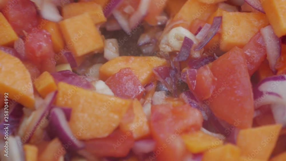 Close-up mixing chopped veggies in a pan, tomato, onion and yams Close-up mixing chopped veggies in a pan, tomato, onion and yams