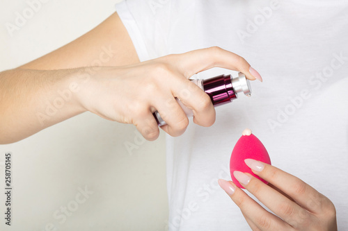 Woman wearing white t shirt applying liquid foundation on a makeup sponge