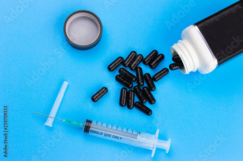 Disposable syringe and pack of black pills on blue background. Сoncept of drug addiction, weight loss, treatment, the danger of medical drugs, death