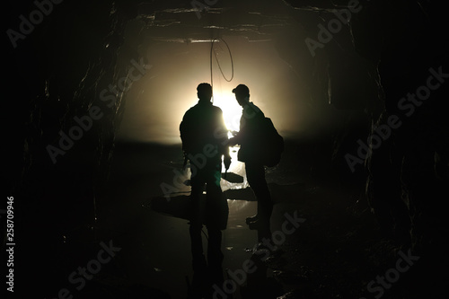 Silhouettes of explorers inside the tunnel of an old abandoned coal mine.