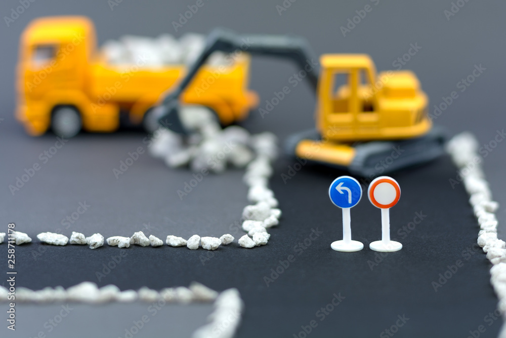Obraz premium Diorama road construction with yellow construction machinery models. Construction concept. Children's toys of construction machinery. Closed road with no entry. Excavator loads stones on truck.