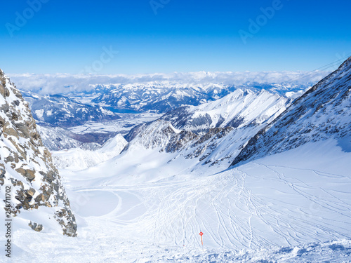Obraz na plátně Winter landscape with free ride piste and view on snow covered slopes and blue sky, with Aerial view of Zell am See lake from the top of Kitzsteinhorn mountain on