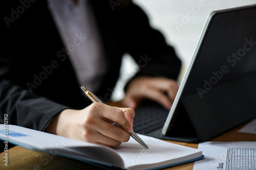 Office staff use laptop computer and note in notebook on desk in office.