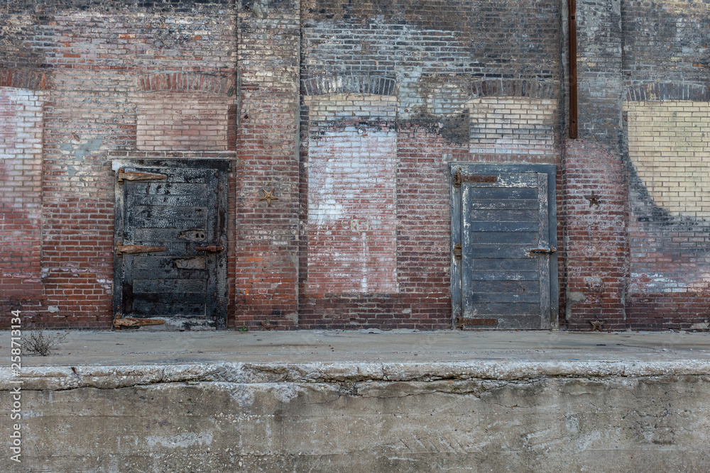 Two large metal doors attached to an abandoned crumbling red brick warehouse Two large metal doors attached to an abandoned crumbling red brick warehouse
