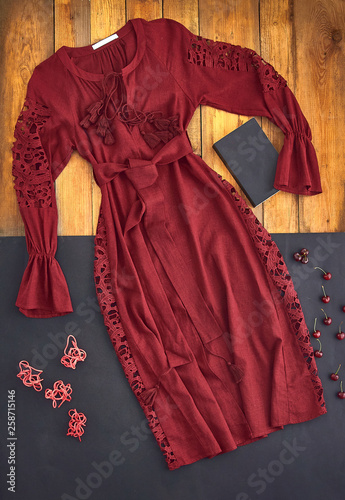 Beautiful unusual outfit presentation for fashion blog, advertising, clothing catalog. Unusual dress burgundy, dark red, cherry, the color of Marsala. Background of parquet boards and black paper.