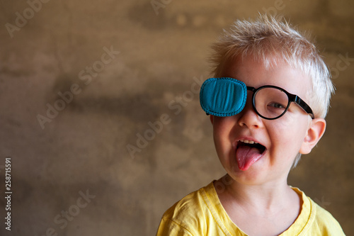 Portrait of funny child in new glasses with patch for correcting squint .Ortopad Boys Eye Patches nozzle for glasses for treatment of strabismus (lazy eye) photo