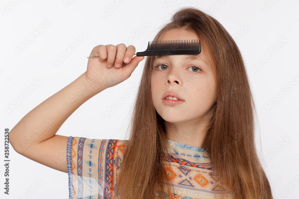 Obraz premium Portrait of an eight-year-old girl who is combing her hair with a comb. Studio photo shoot on a white background
