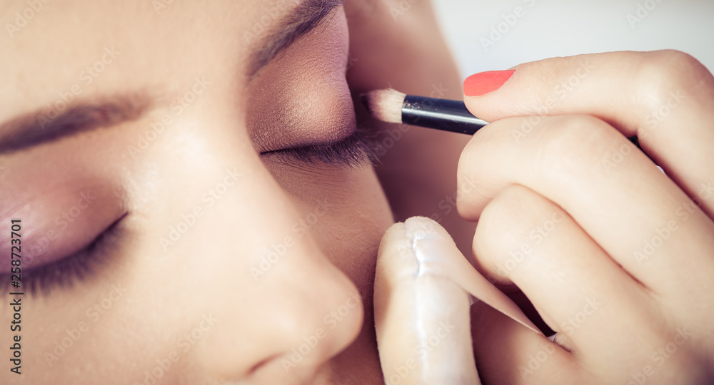 Closeup of hands applying eyeshadow powder on female facial skin