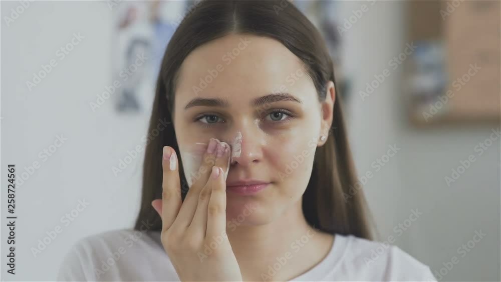 Woman applying mask moisturizing skin cream on face and look at the camera Woman applying mask moisturizing skin cream on face and look at the camera