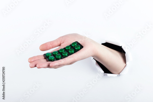 Female hand out of the hole in the paperman, holding blisters with pills. Isolate on white background. photo