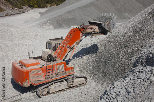 Large red excavator loads gravel in a bucket, view from above, closeup. Quarry equipment. Mining industry.
