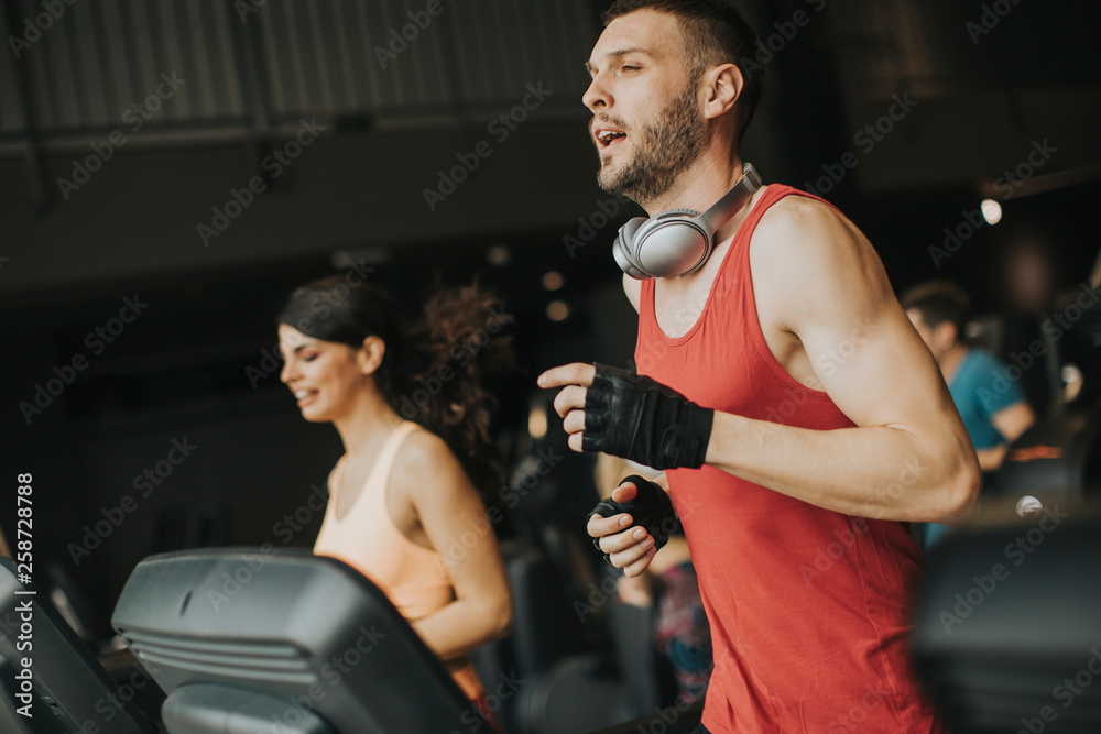 Young couple running on treadmills in modern gym Young couple running on treadmills in modern gym