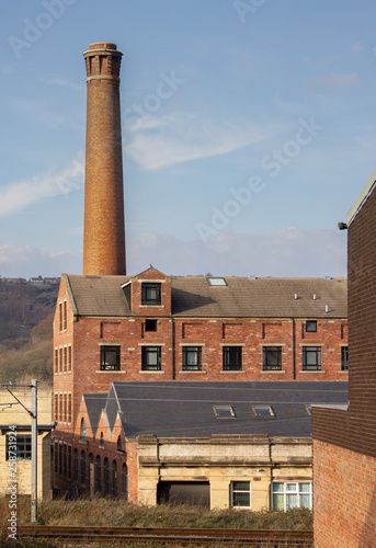 A Victorian mill with large chimney towers over a railway line