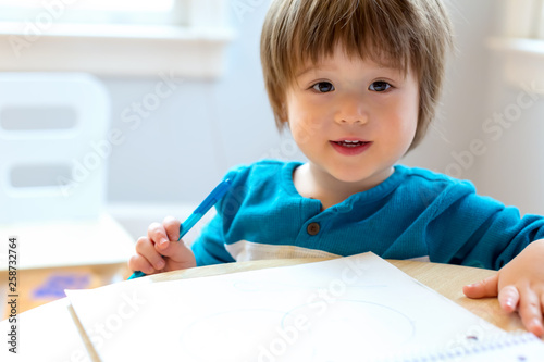 Happy toddler boy drawing at his desk