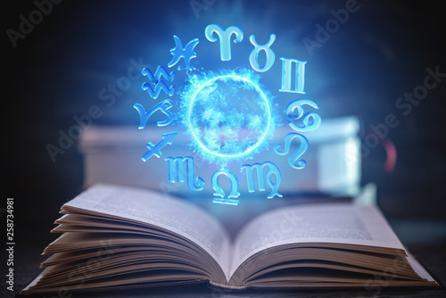 Fototapeta Naklejka Na Ścianę i Meble -  Open book on astrology on a dark background. Glowing magical globe with signs of the zodiac in the blue light.