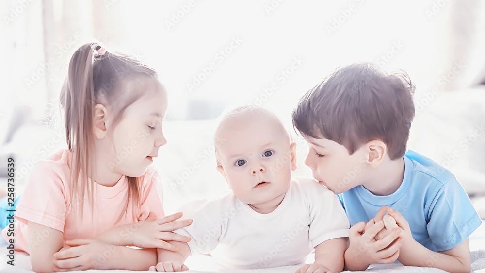 Children lie on the bed next to the newborn baby, little sister. Children lie on the bed next to the newborn baby, little sister.