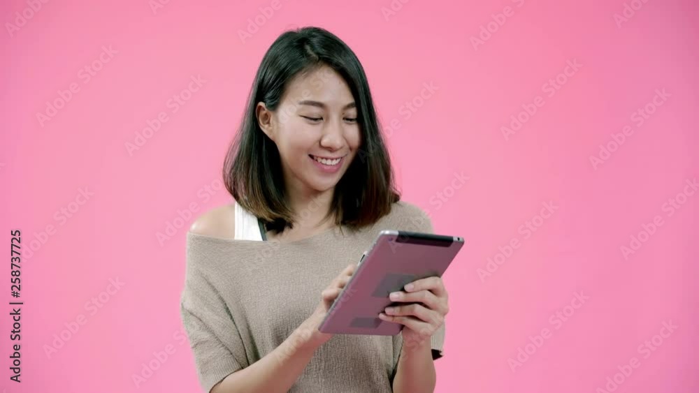 Young Asian woman using tablet buying online shopping by credit card feeling happy smiling in casual clothing over pink background studio shot. Happy smiling adorable glad woman rejoices success. Young Asian woman using tablet buying online shopping by credit card feeling happy smiling in casual clothing over pink background studio shot. Happy smiling adorable glad woman rejoices success.