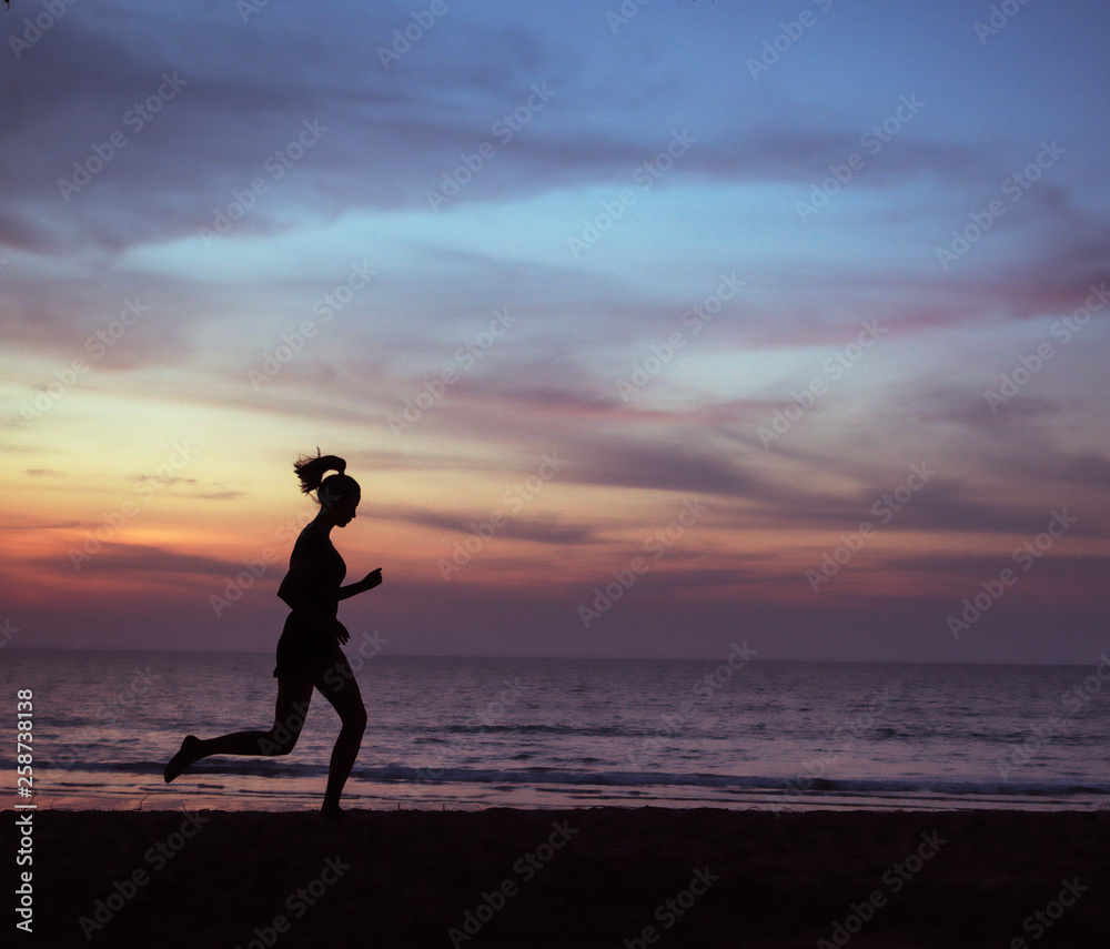 Young, athletic lady jogging on a beach during the susnet