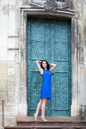Young girl posing in a blue dress for the camera on a background of green metal door. Confident stylish woman looks to the side