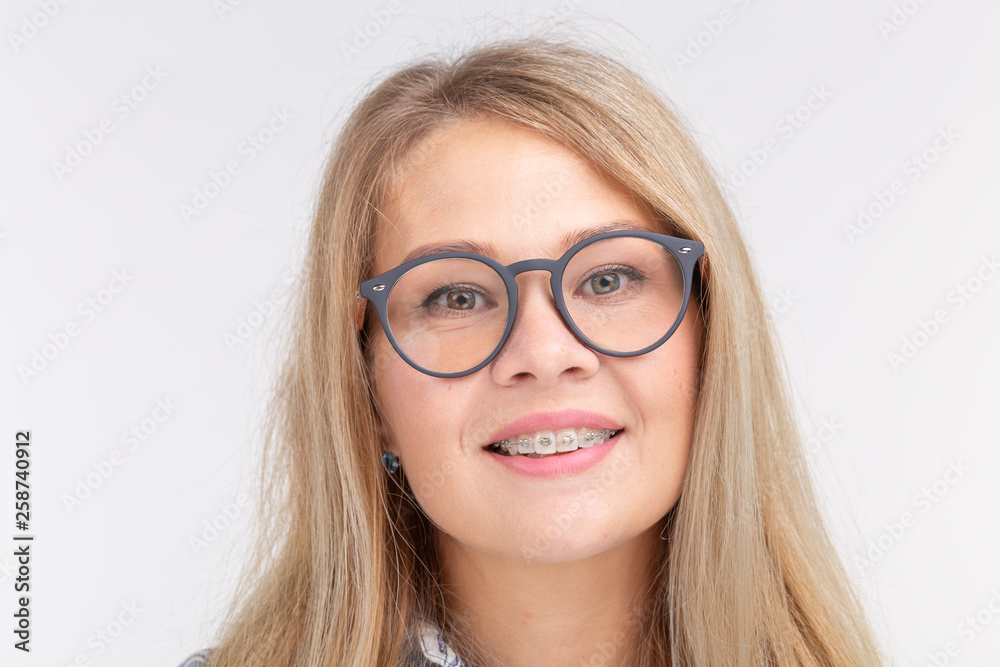 Teeth health, dentistry and bite correction - Happy smiling woman in glasses with braces on white background Teeth health, dentistry and bite correction - Happy smiling woman in glasses with braces on white background