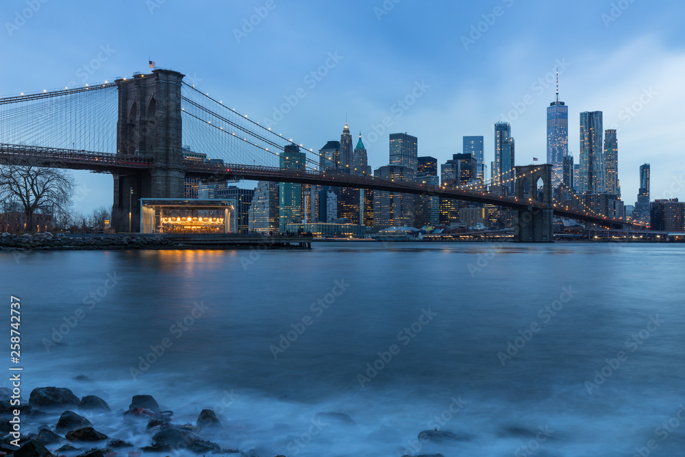 Brooklyn Bridge in Manhattan downtown with Cityscape on a foggy cloudy day at sunset New York USA