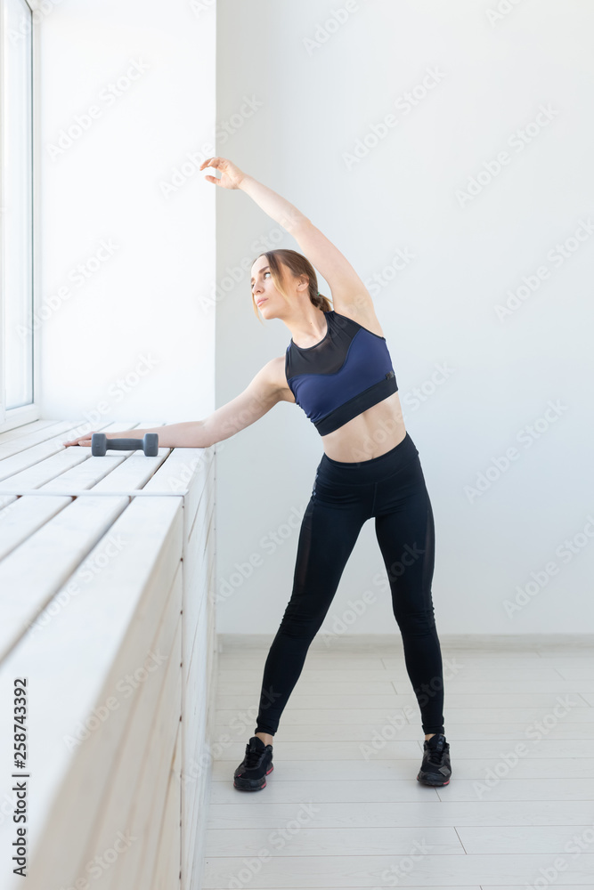 People, sport and fitness concept - young woman doing exercises stretching near window People, sport and fitness concept - young woman doing exercises stretching near window