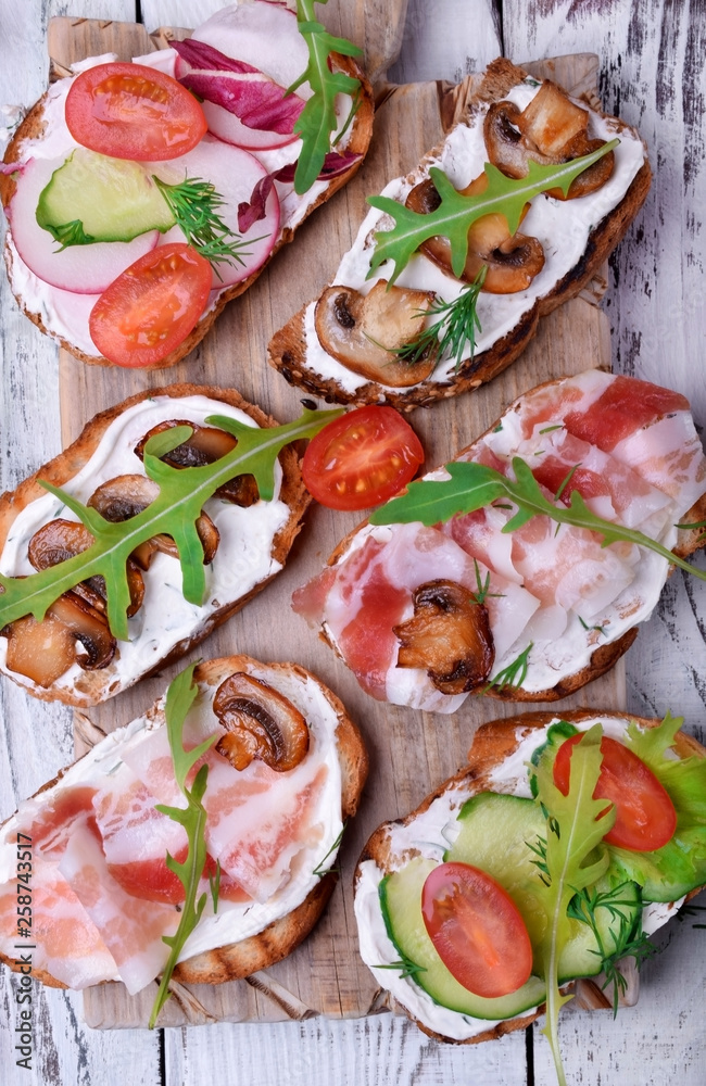 Bruschetta assortment with cream cheese, champignons, pancetta meat, vegetables and greenery Bruschetta assortment with cream cheese, champignons, pancetta meat, vegetables and greenery