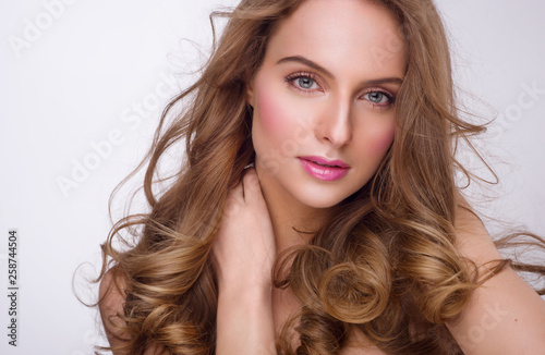 Attractive young woman with blue eyes, clean fresh skin and long flattering hair. Touching neck with a hand. Shiny natural make up. Studio white, horizontal shot