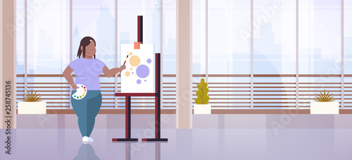 fatty obese woman painter holding paintbrush african american overweight girl artist painting process art workshop studio interior full length flat horizontal