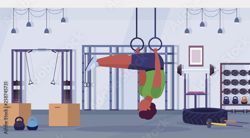 sporty man doing ring dips exercises with gymnastic rings african american guy training cardio crossfit workout concept modern gym health club studio interior horizontal full length