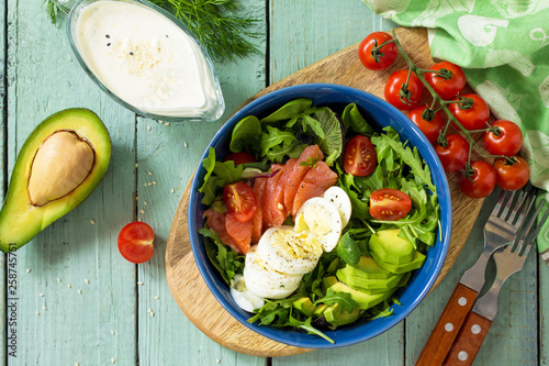 Diet menu, Vegan food. Healthy salad with arugula, Tomatoes, Salmon, Egg and Avocado on wooden table. Top view flat lay background.