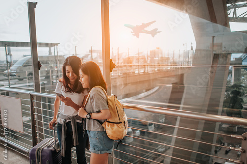 girls using smartphone checking flight or online check-in at airport together, with luggage. Air travel, summer holiday, or mobile phone application