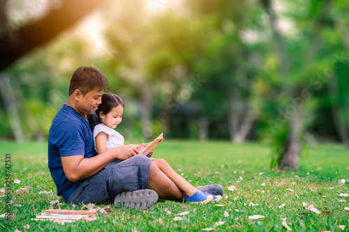 father sitting on grass with little daughter and reading book story in the park