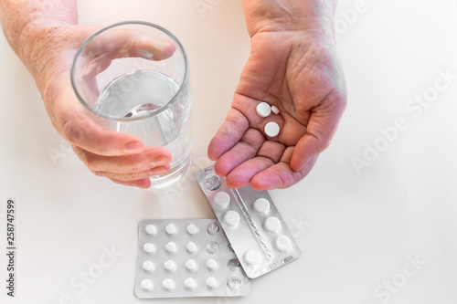 Hands of an elderly person with pills  packaging of medication. Glass of water. The concept of maintaining life in old age  treatment and health.